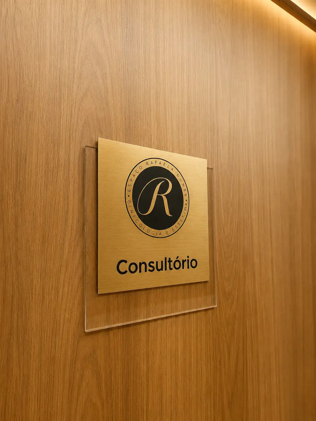 Placa dourada com o monograma da Dra. Rafaela Nunes indicando a porta do consultório