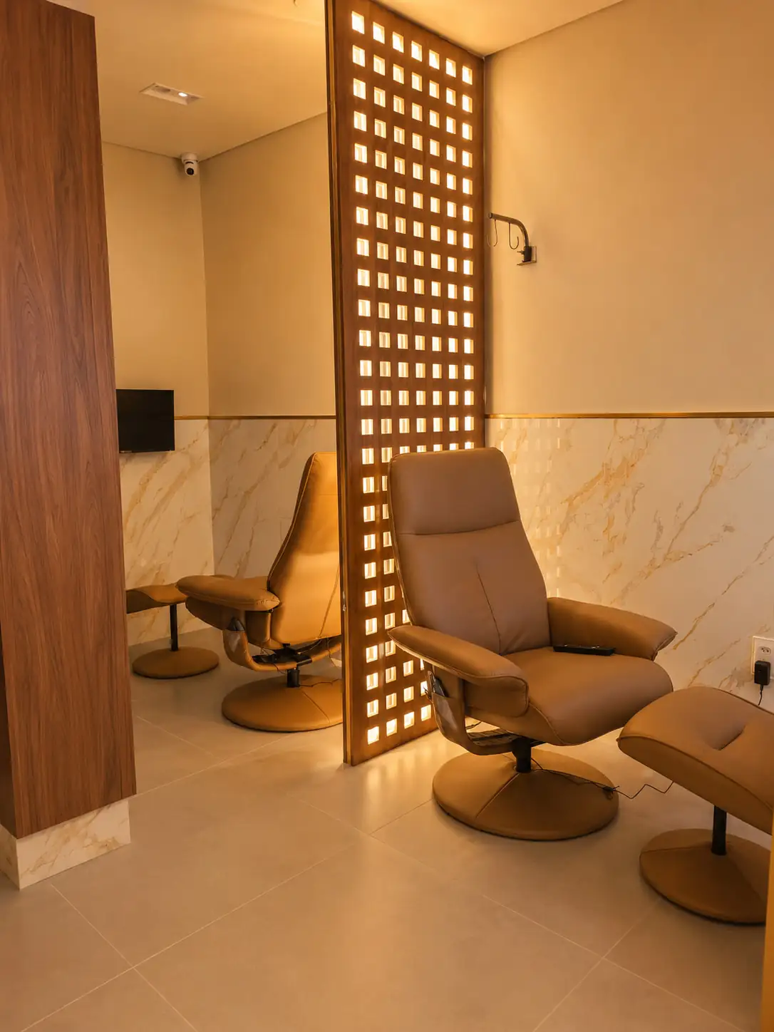 Sala de recuperação com poltronas reclináveis separadas por painel vazado iluminado